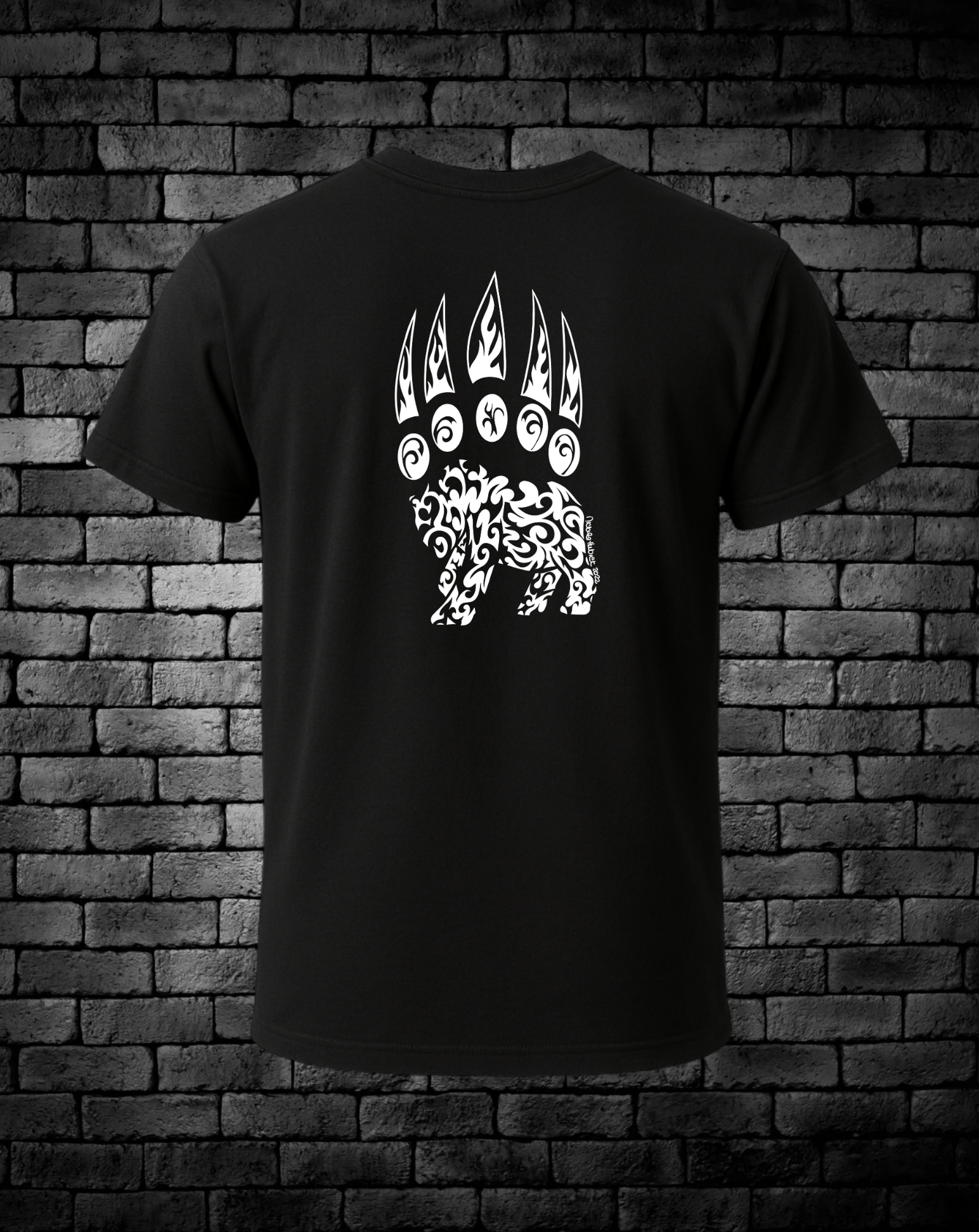 Black t-shirt with a hand-drawn white bear paw design on the back, against a brick wall background.