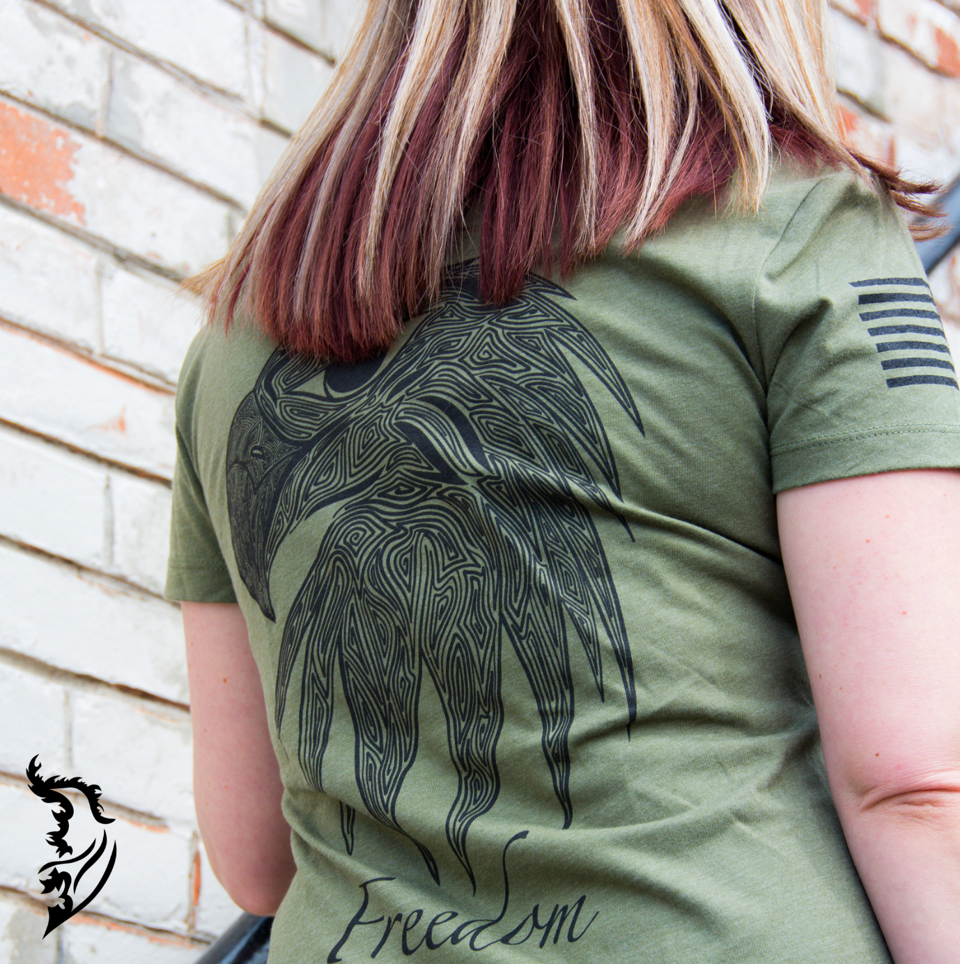 Back view of a military green ladies tee featuring an intricate eagle head design with 'Freedom' text below, embodying strength and patriotism.