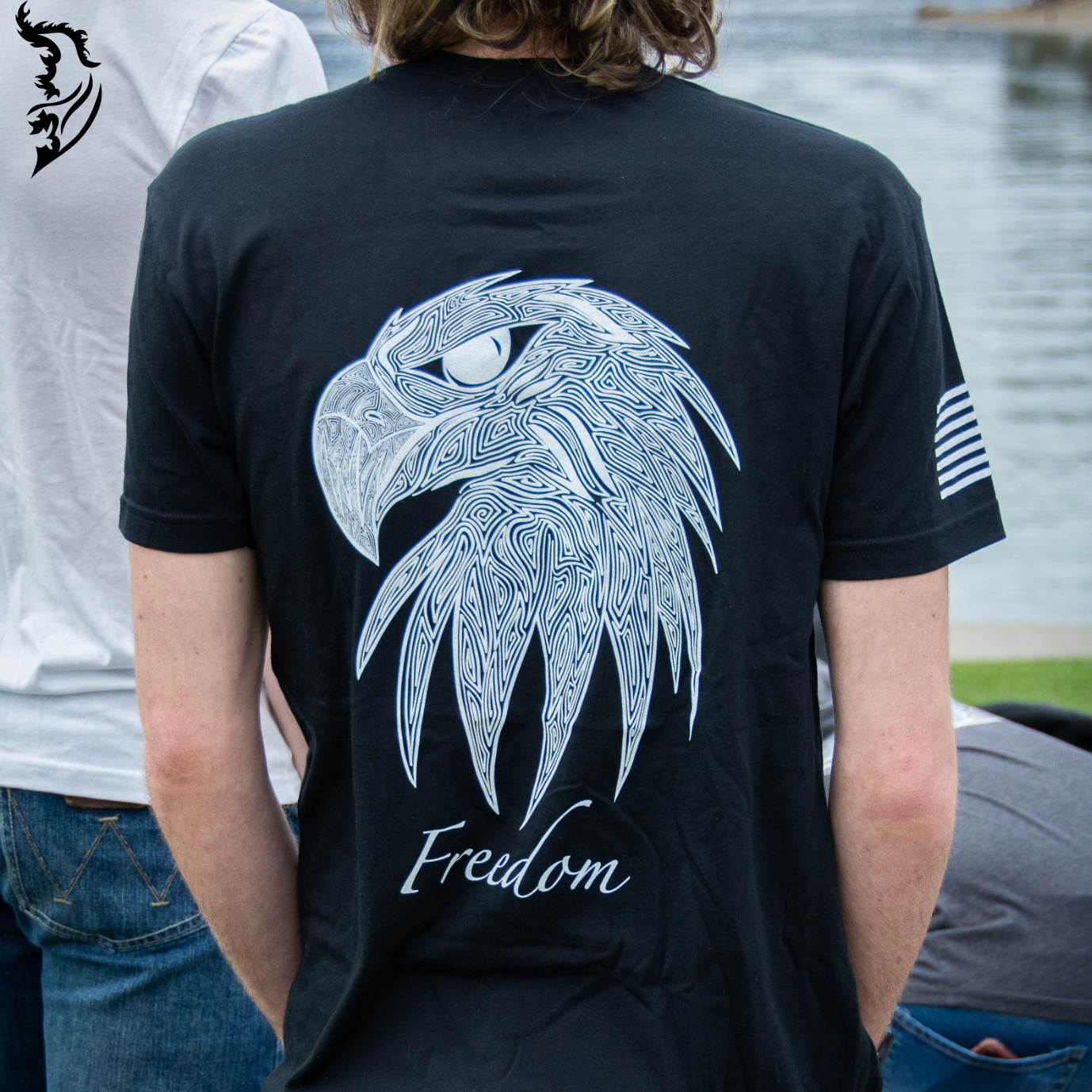Hand-drawn eagle head with fine linework and 'Freedom' text featured on a black t-shirt, with brand logo on the chest.