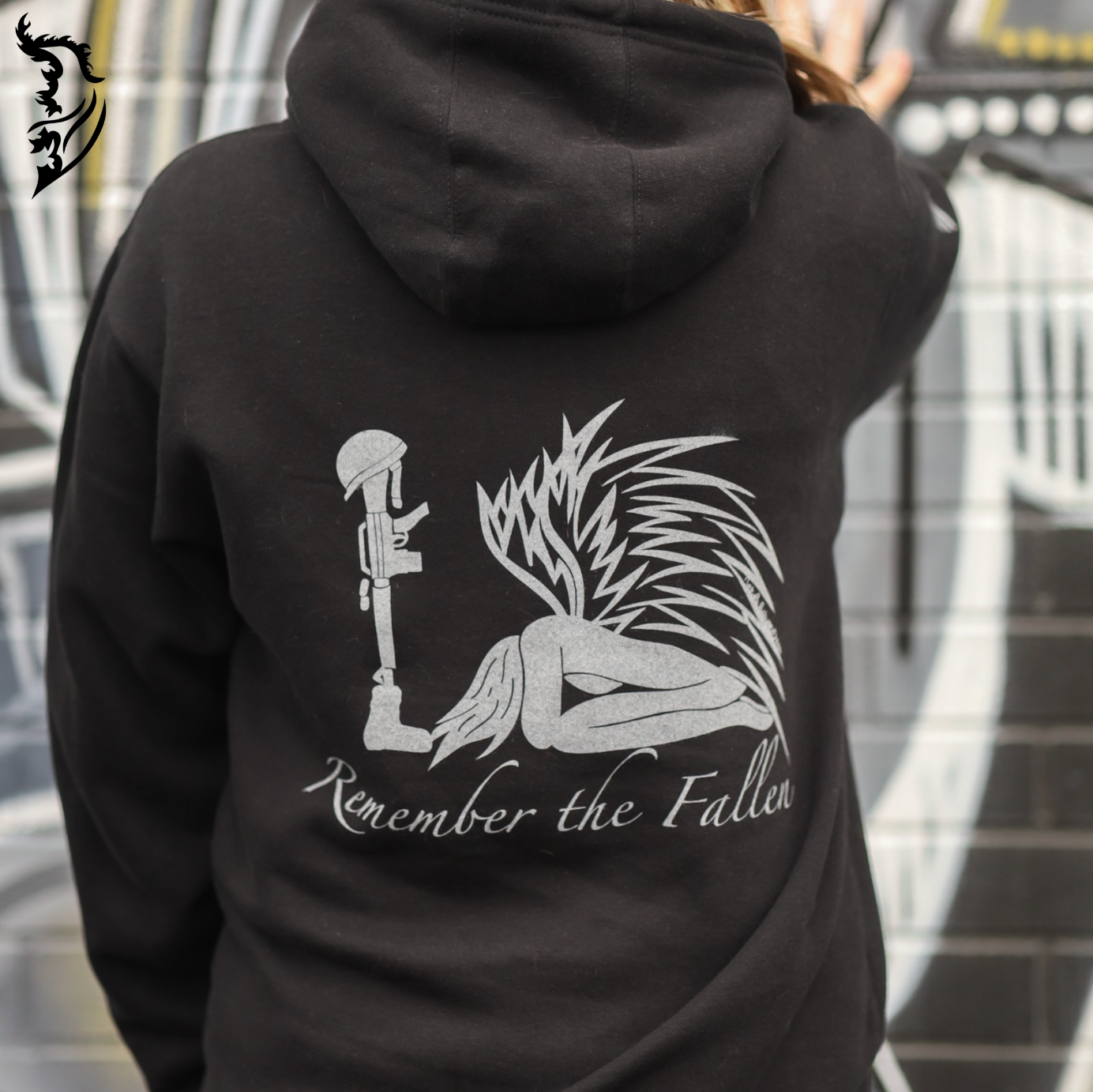 Back view of a black fleece-lined hoodie featuring a kneeling angel with extended wings, honoring fallen soldiers with a battlefield cross.