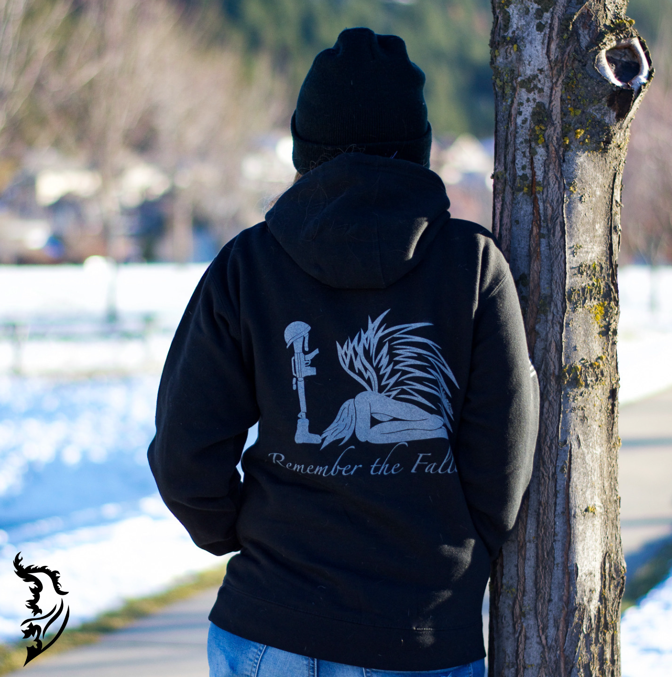 Black hoodie showcasing an intricate angel with outstretched wings, bowing before a soldier’s boot, rifle, and helmet in tribute.