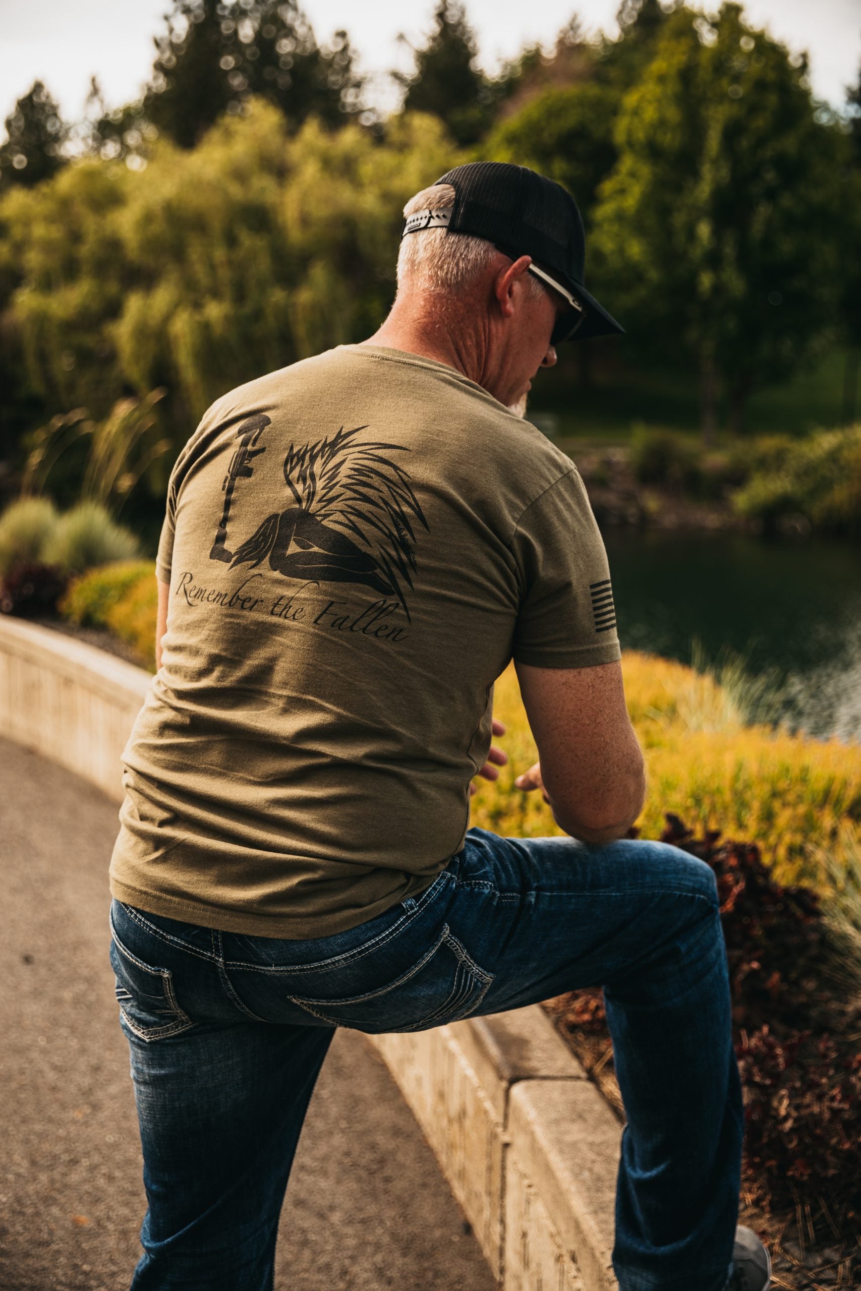 Back view of a men's tee featuring a hand-drawn angel kneeling with wings extended, before a soldier’s boot, rifle, helmet, and dog tags in tribute to fallen soldiers.