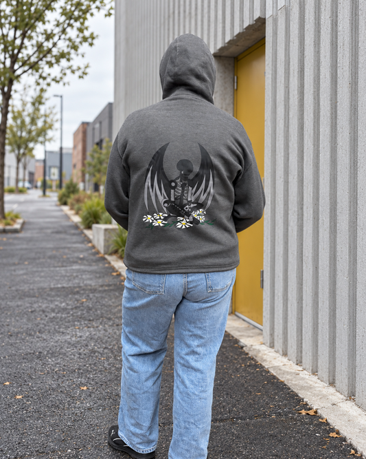 Back view of a person wearing a charcoal gray hoodie with a hand-drawn winged mechanical skeleton and white daisy design, paired with light blue jeans, beside a ribbed concrete building with a yellow door.