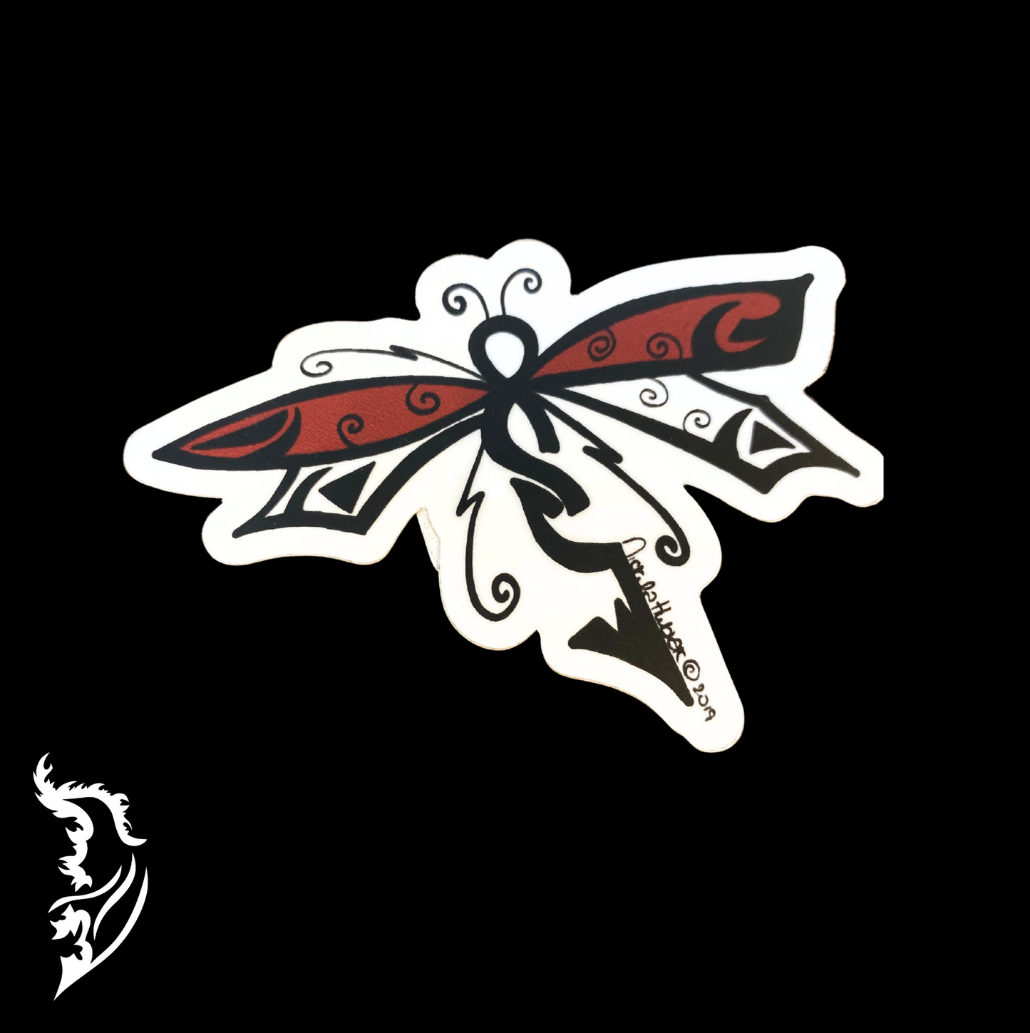 Hand-drawn red and black dragonfly vinyl sticker with decorative swirling wing details on a dark background.