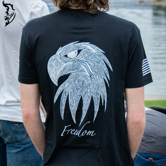 Hand-drawn eagle head with fine linework and 'Freedom' text featured on a black t-shirt, with brand logo on the chest.