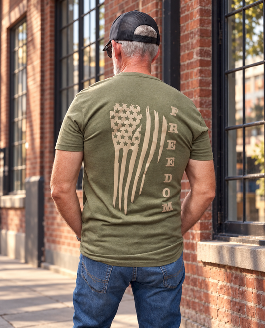 Back view of the military green Freedom Flag T-shirt featuring a large distressed American flag and vertical “FREEDOM” lettering in tan