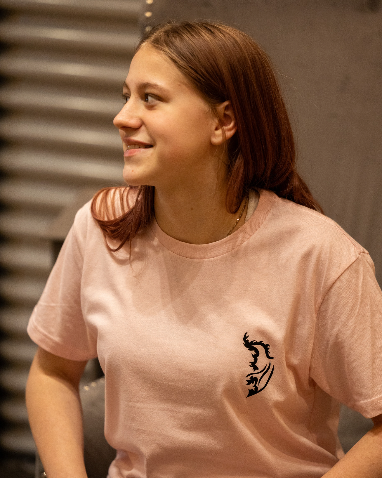 Person wearing a pale pink t-shirt with a black Angel Wing logo on front left chest