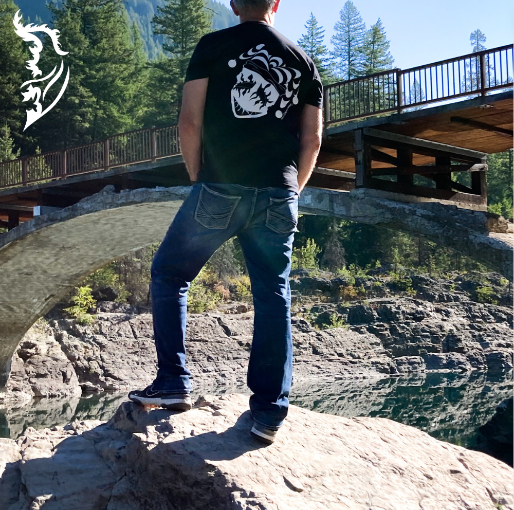 Male model wearing joker tee standing on rocks by a river