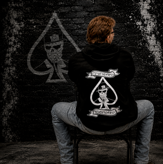 Man wearing black “Live Hard Play Hard” hoodie by Street Style by Nickola sitting against a gritty black brick wall 