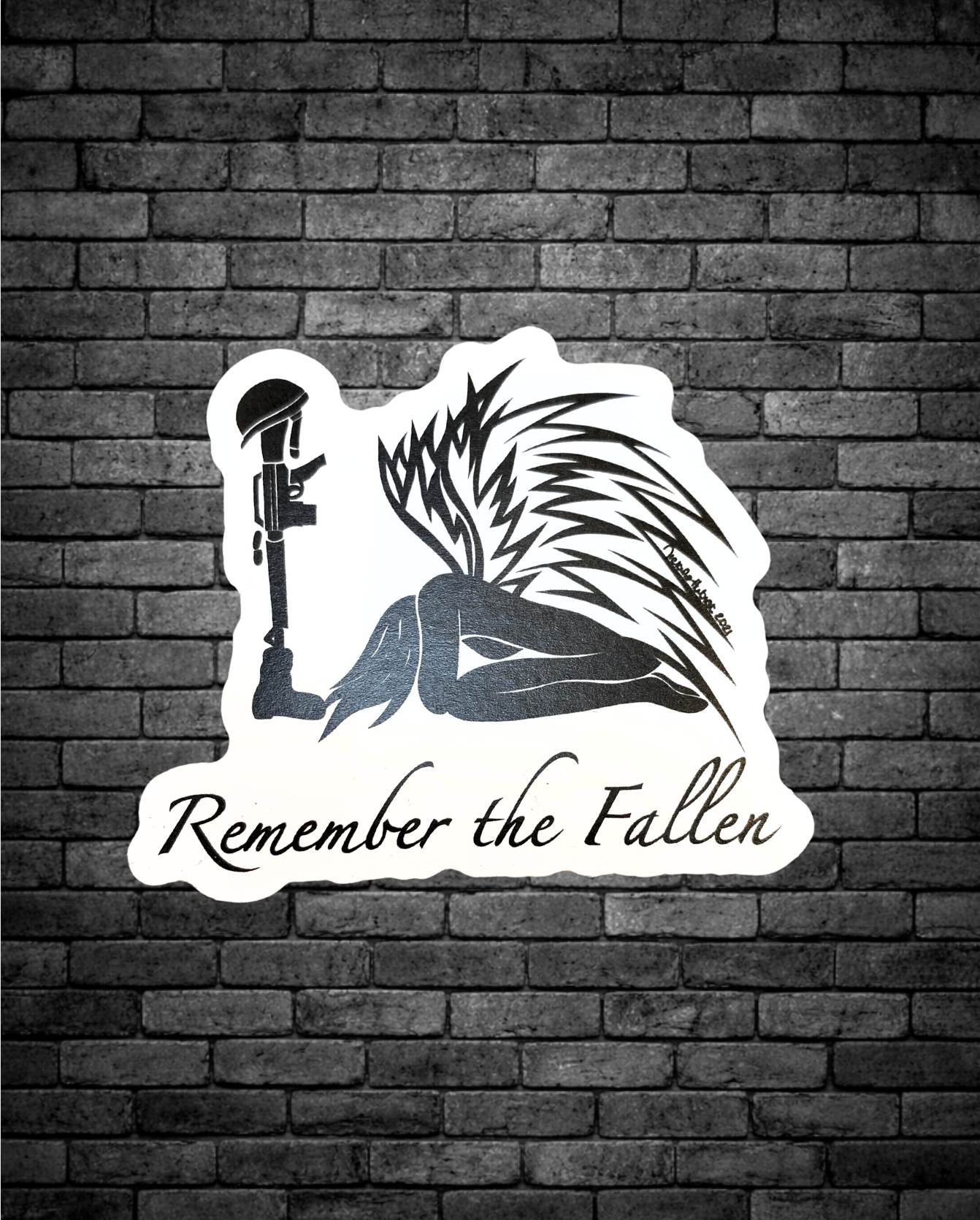  The design features a kneeling angel with detailed wings beside a rifle topped with a helmet, with the words “Remember the Fallen” written beneath. 