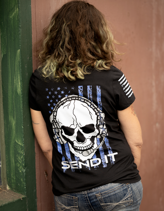 “5'6" female model wearing a size small black JTAC Send It T-shirt with skull headset and blue distressed flag artwork on the back.”