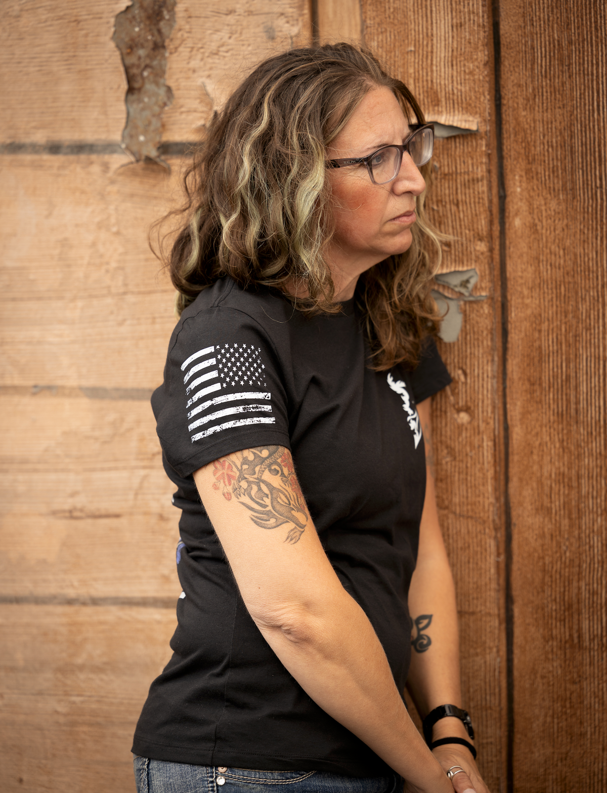 “5'6" female model wearing a size small black JTAC Send It T-shirt with a distressed American flag printed on the sleeve.”
