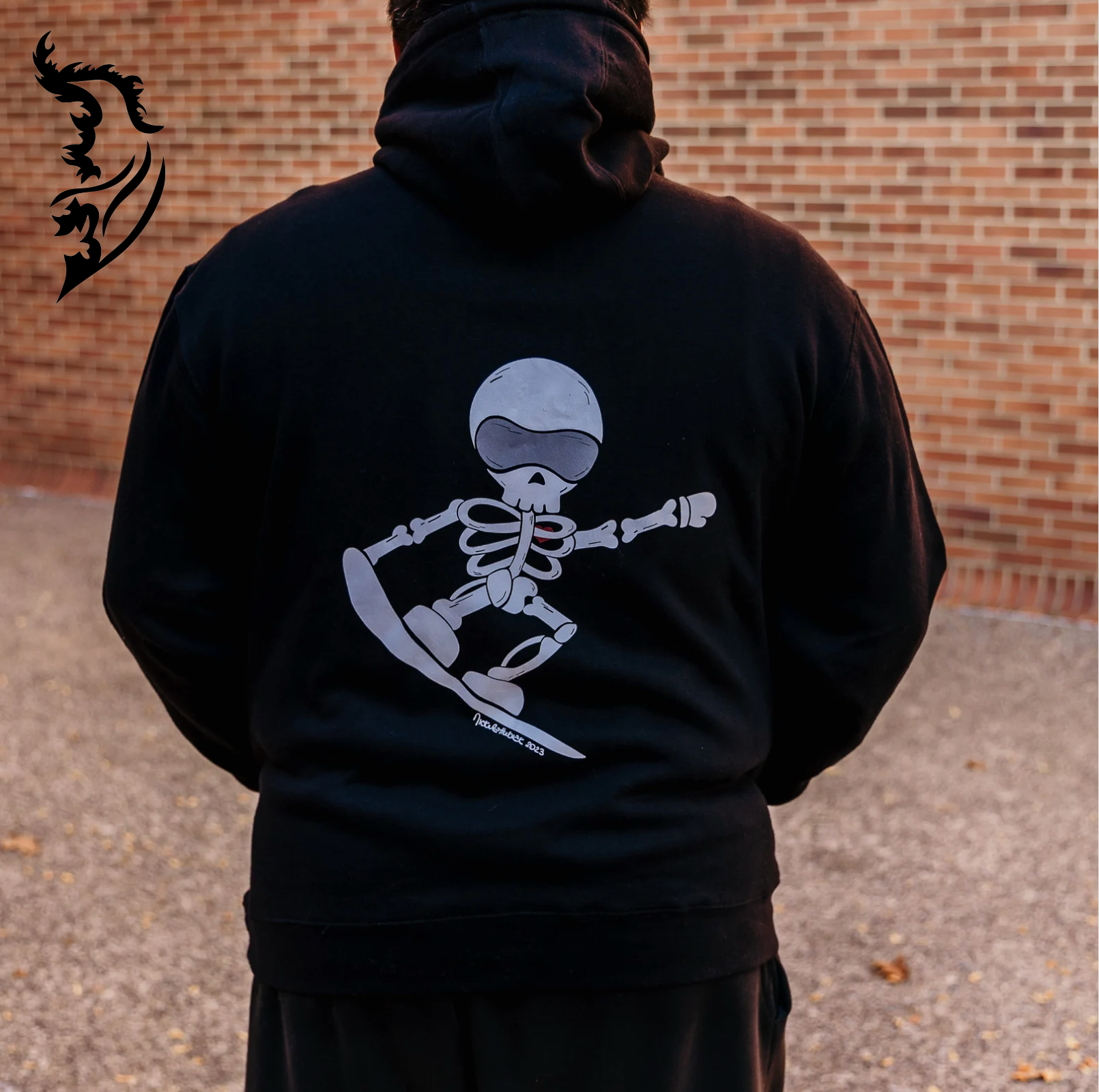 Black fleece-lined hoodie featuring hand-drawn skeleton with a red heart on the back center and angel wing logo on the front left chest. Stylish wearable art perfect for bold personal expression and street style fashion enthusiasts. Unique and trendy design for artistic clothing lovers.