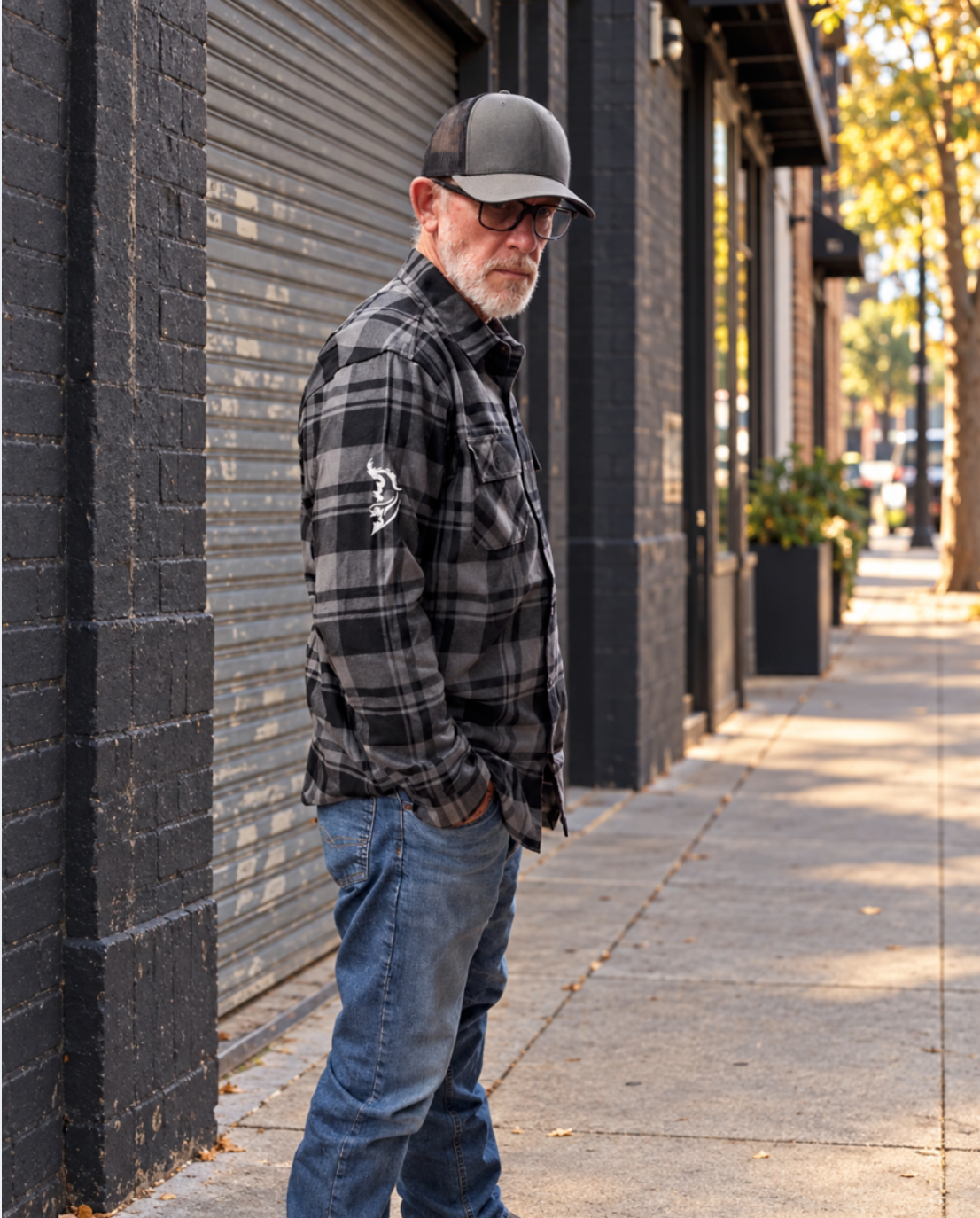 Side view of the gray and black plaid stag flannel, showing its collar, chest pocket, and white Angel Wing logo on the sleeve as the model stands on a city sidewalk.