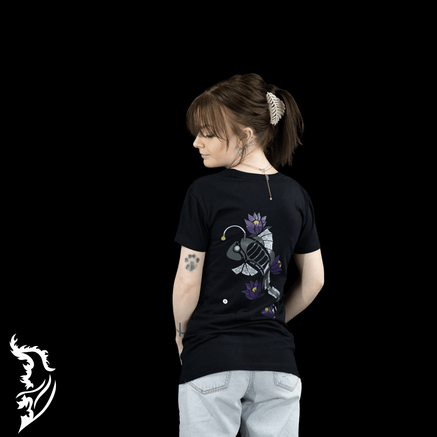 Woman wearing a black Street Style by Nickola slim-fit T-shirt featuring a hand-drawn steampunk fish design with purple lotus flowers on the back, photographed against a dark background.