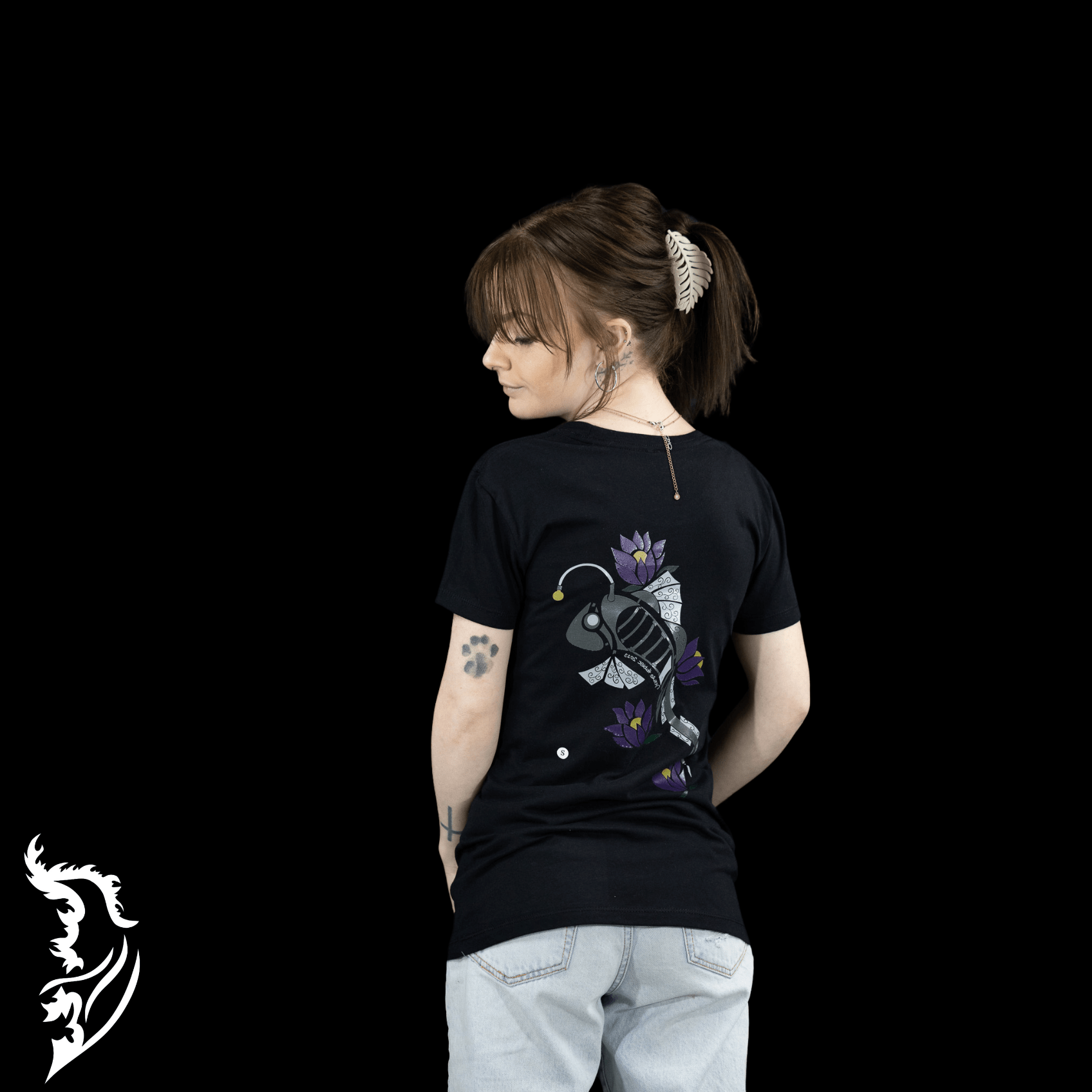 Woman wearing a black Street Style by Nickola slim-fit T-shirt featuring a hand-drawn steampunk fish design with purple lotus flowers on the back, photographed against a dark background.