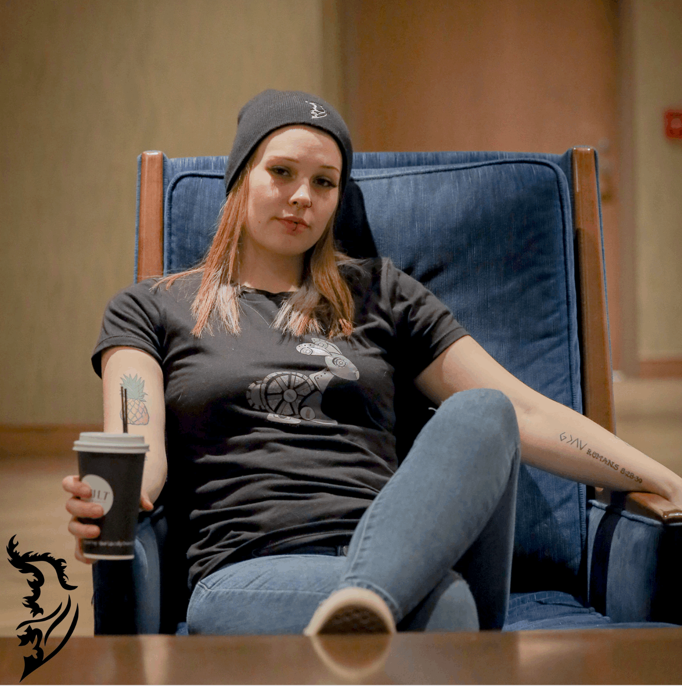 Woman wearing a black Street Style by Nickola T-shirt featuring a hand-drawn steampunk rabbit design on the front, sitting in a blue chair holding a coffee cup.