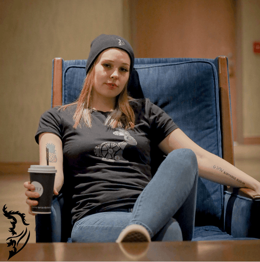 Woman wearing a black Street Style by Nickola T-shirt featuring a hand-drawn steampunk rabbit design on the front, sitting in a blue chair holding a coffee cup.