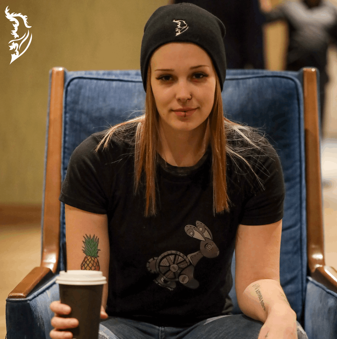 Woman wearing a black Street Style by Nickola T-shirt featuring a hand-drawn steampunk rabbit design on the front, sitting in a blue chair holding a coffee cup.